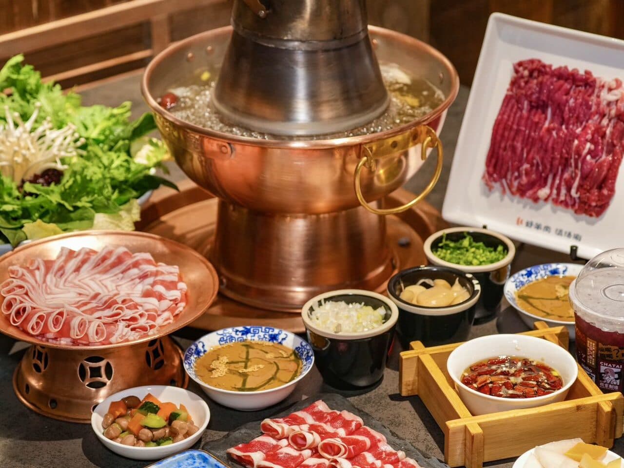 A copper hotpot table: the pot with hand-cut mutton, mushrooms and greens, and several dipping sauces