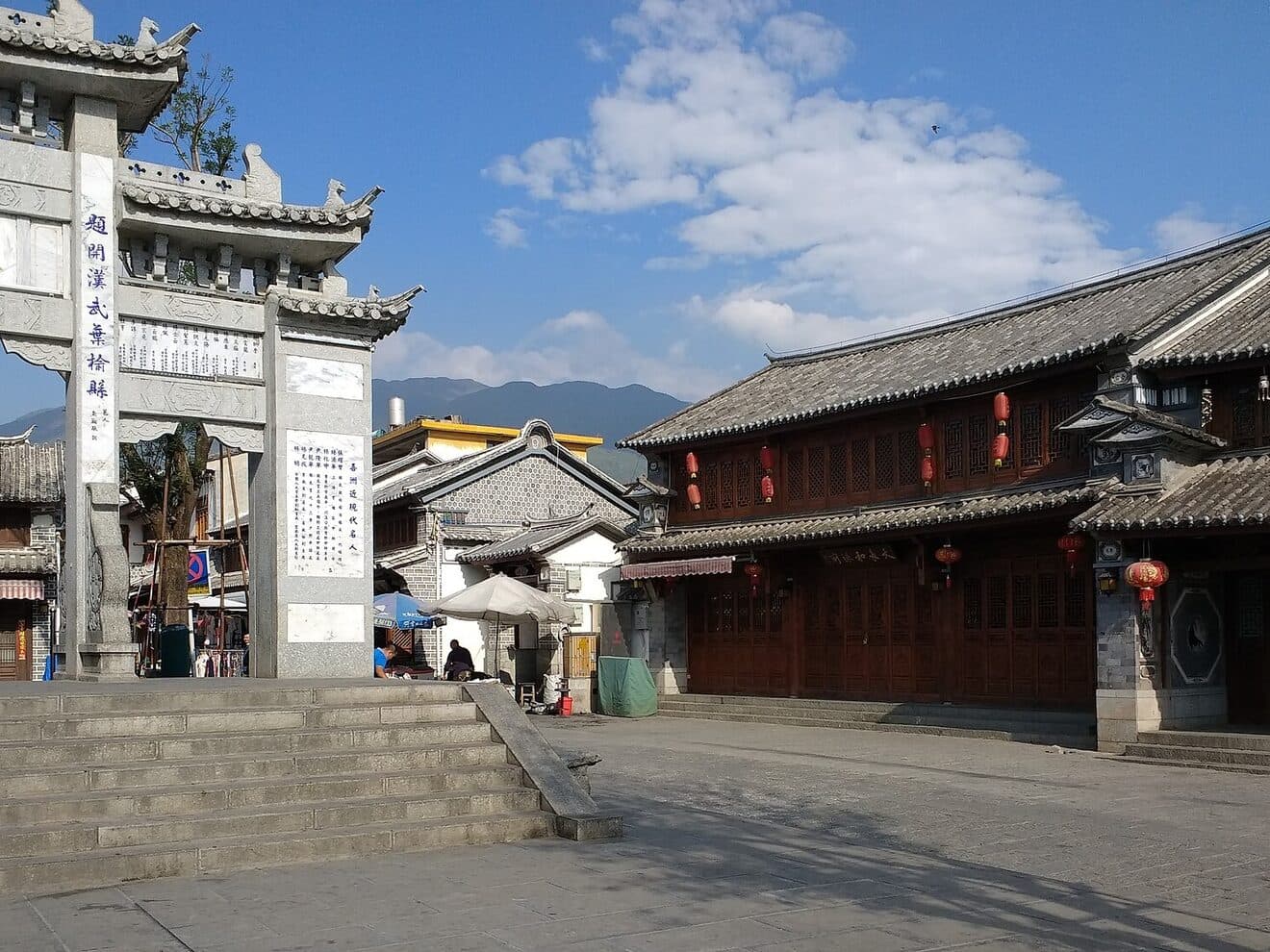 The centre of a Bai town: a timber archway with white-walled, grey-tiled houses and painted eaves around a small square
