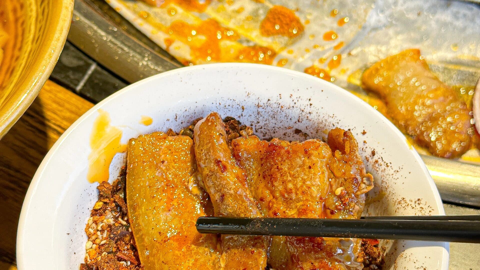 Golden grilled milk-fan slices dipped in dry chilli, one lifted with chopsticks and more grilling on the griddle