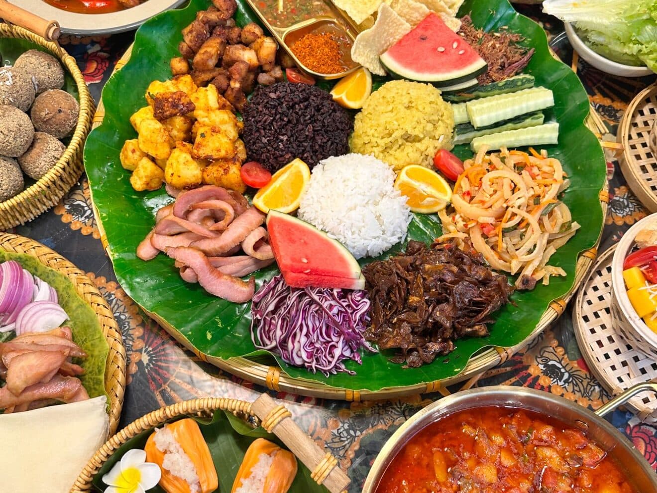 A Yunnan platter on banana leaves: purple rice, pumpkin and fried dishes beside a soup pot