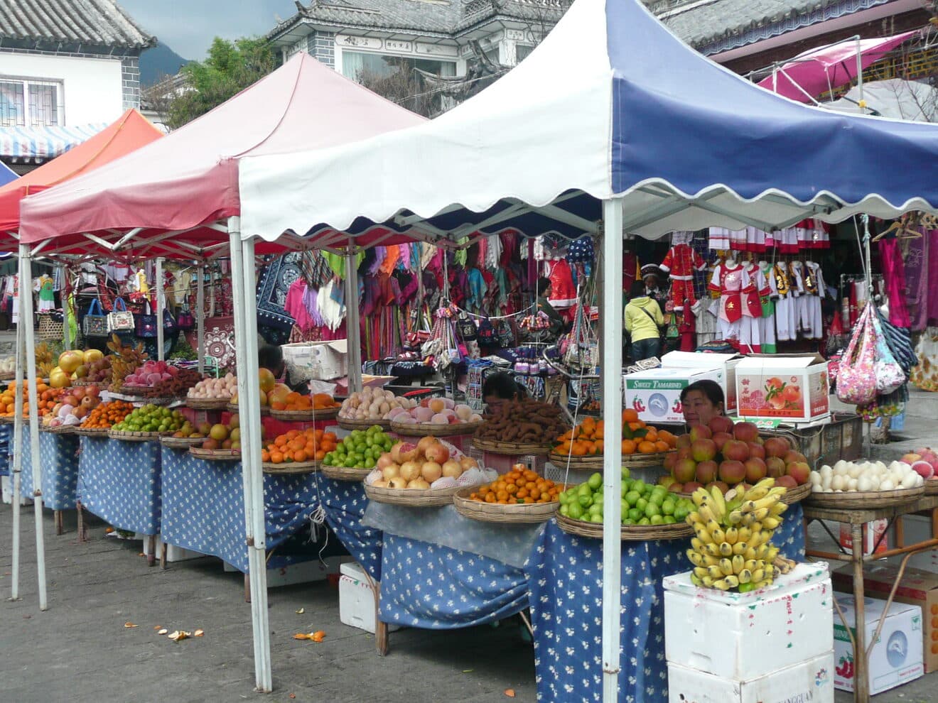 A morning market in Dali old town: fruit and vegetable stalls under a run of canopies, produce heaped and scales on the tables