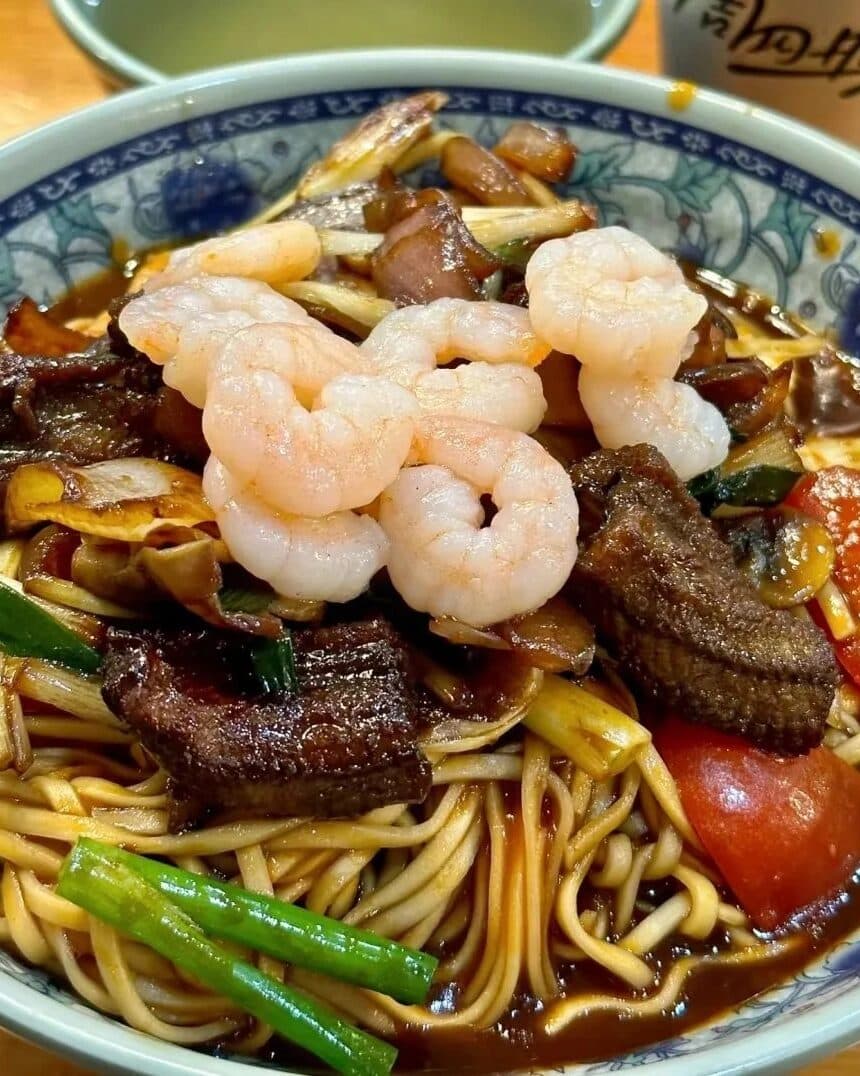 A blue-and-white bowl of noodles with shrimp, mushrooms and greens
