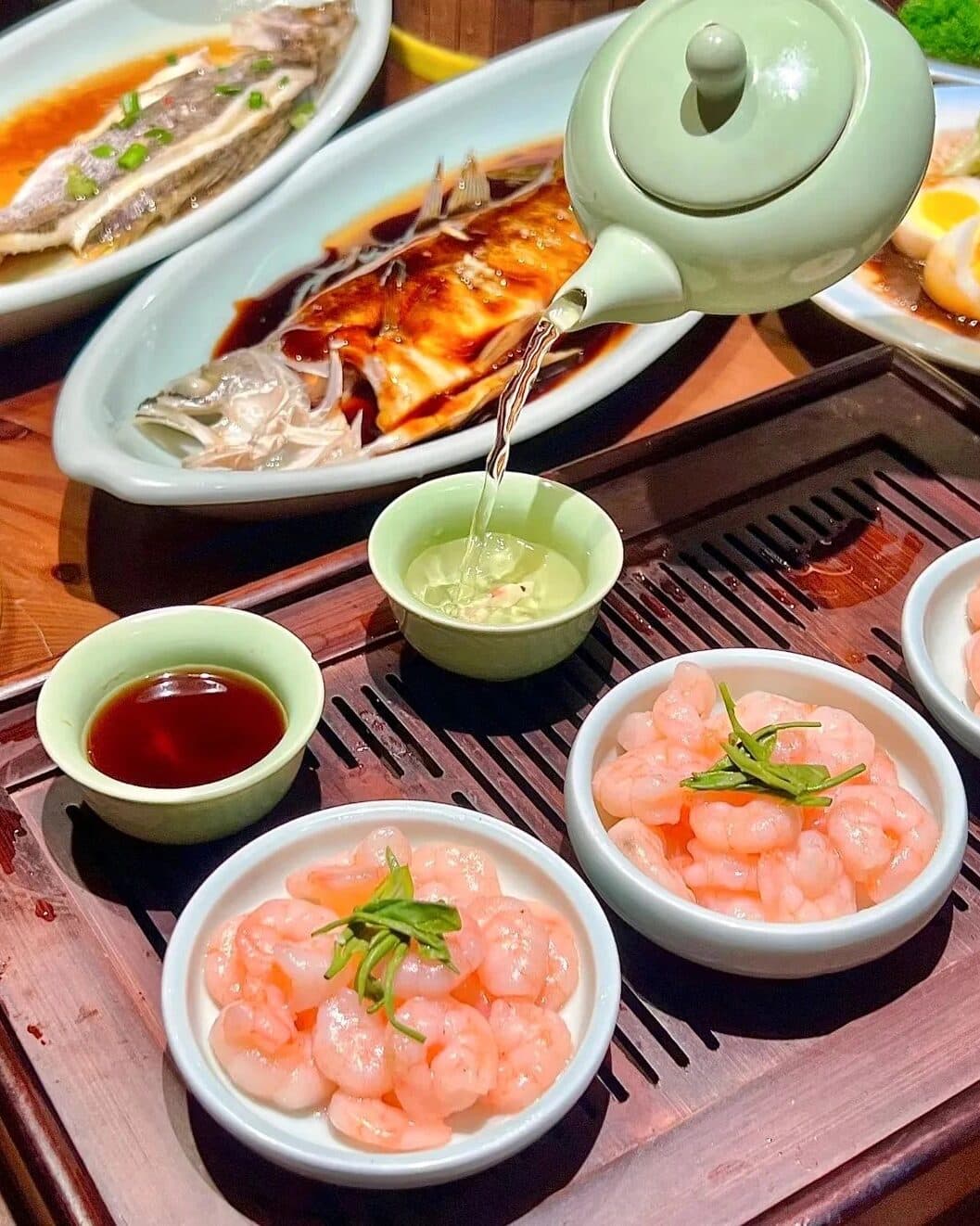 Stir-fried shrimp on a wooden tray with a teapot pouring tea, a cup and a dipping dish