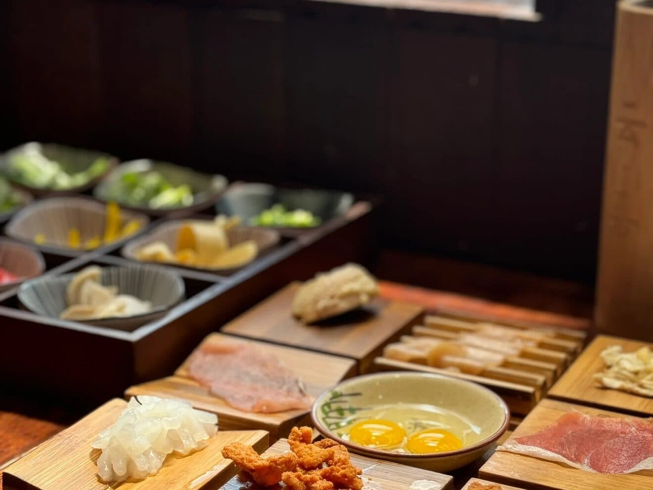 Wooden trays of crossing-the-bridge noodle side dishes: small plates of meat, vegetables and egg