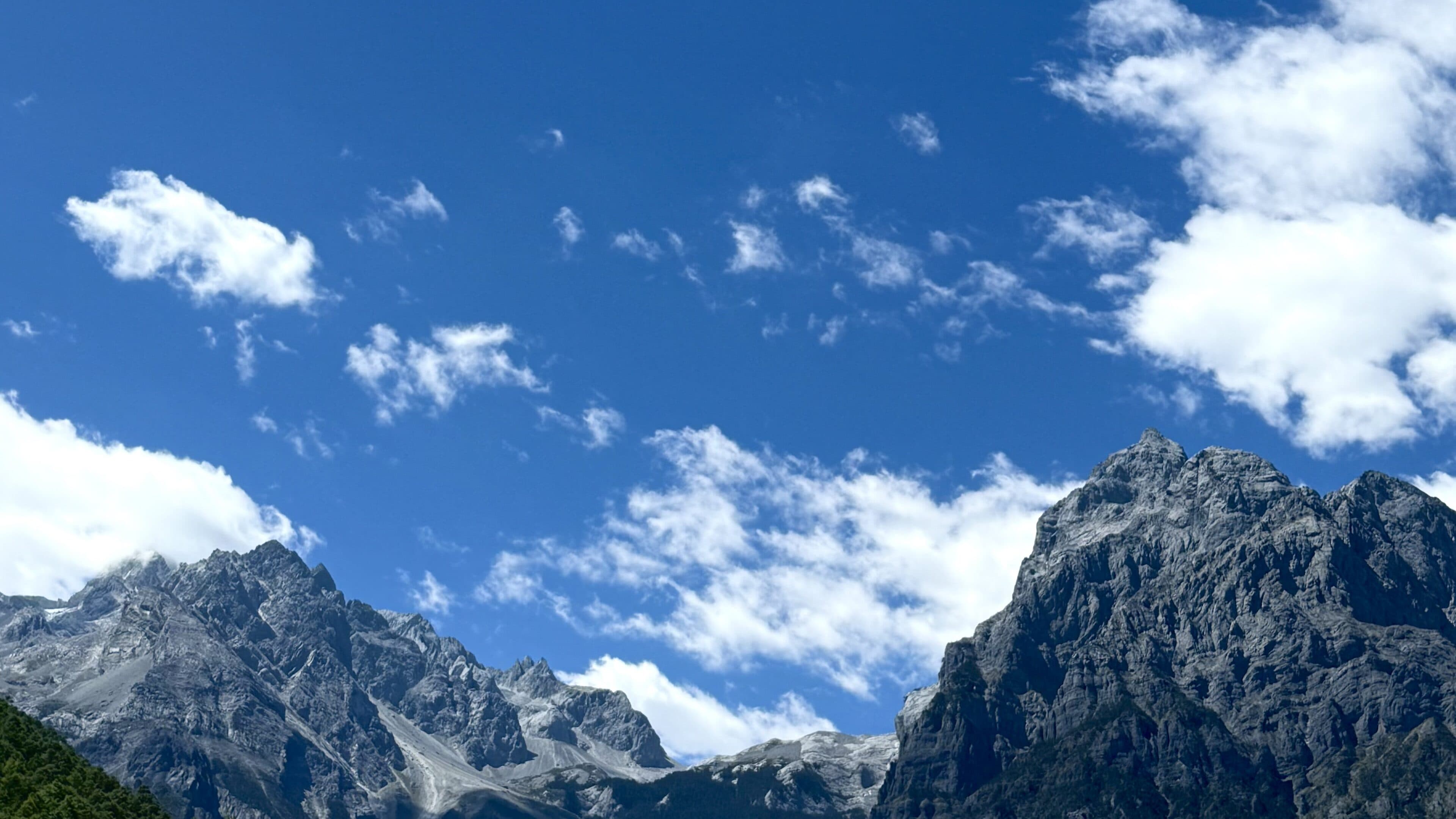Dark rocky peaks with patches of snow under wide blue sky and cloud