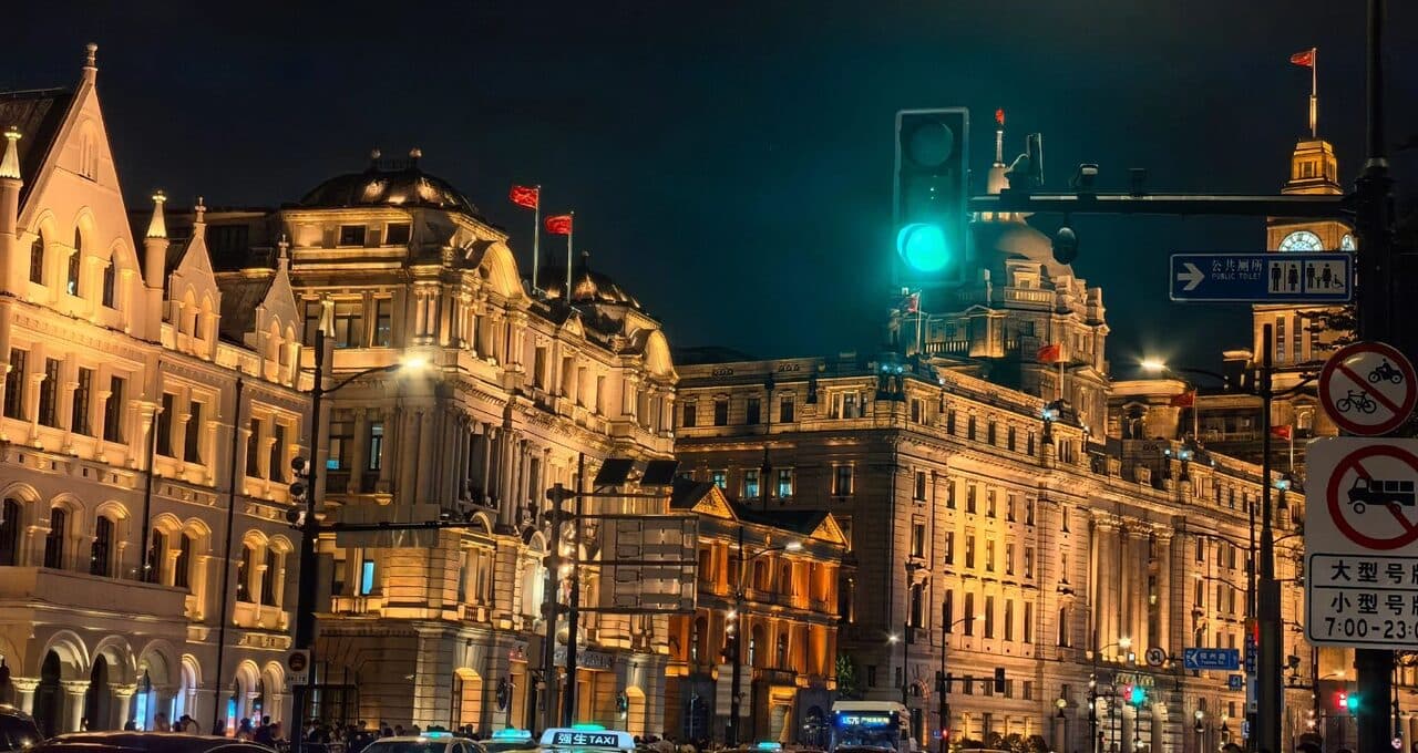 The Bund's historic facades at night, with street trees and traffic along the road