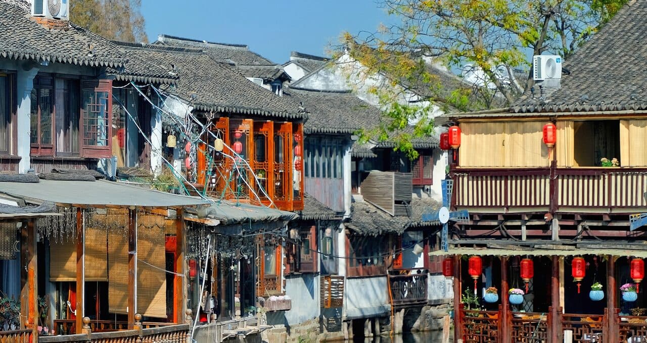 A canal lane in the Pingjiang Road area: timber shopfronts and red lanterns along the water, tour boats moored on the canal