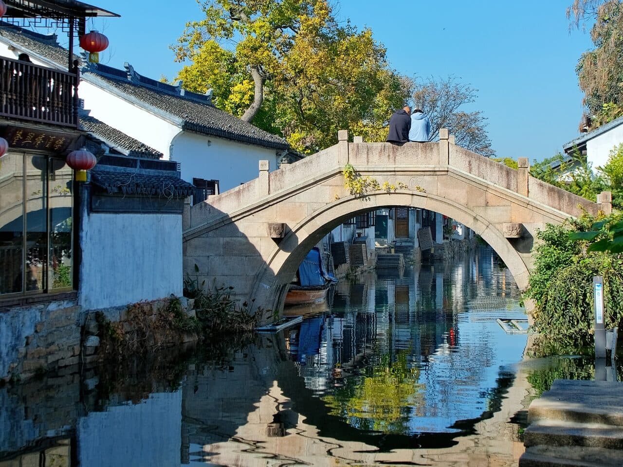 A stone arch bridge over a canal, its arch mirrored in the water, with whitewashed houses on both banks