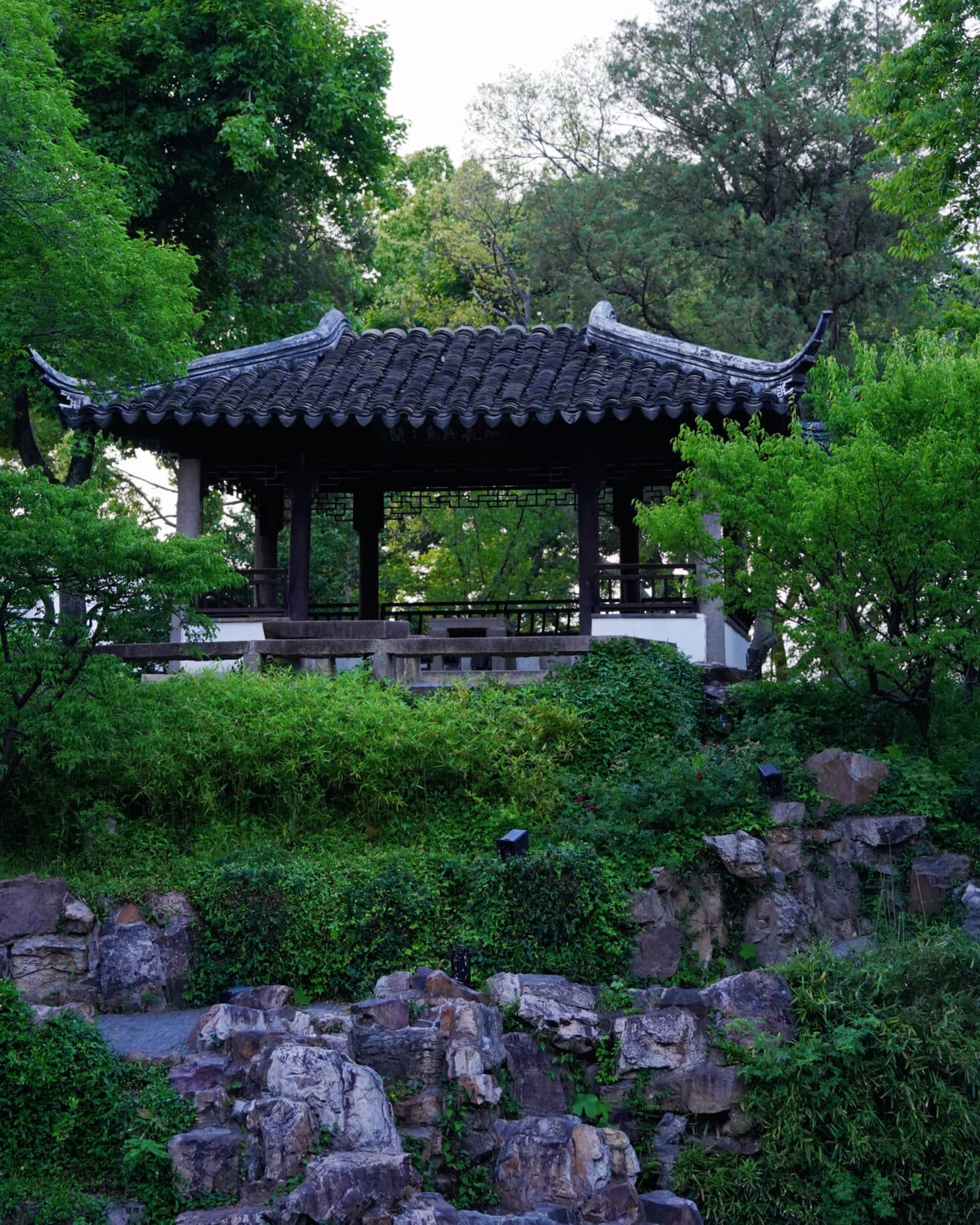 A garden pavilion and stacked rockery framed by evergreens and white walls
