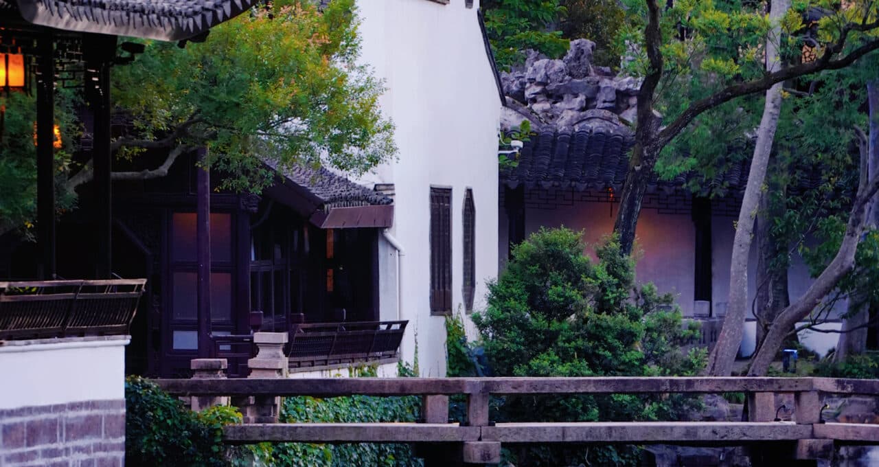 A garden pond with a white-walled hall, rockery and planting on the far bank