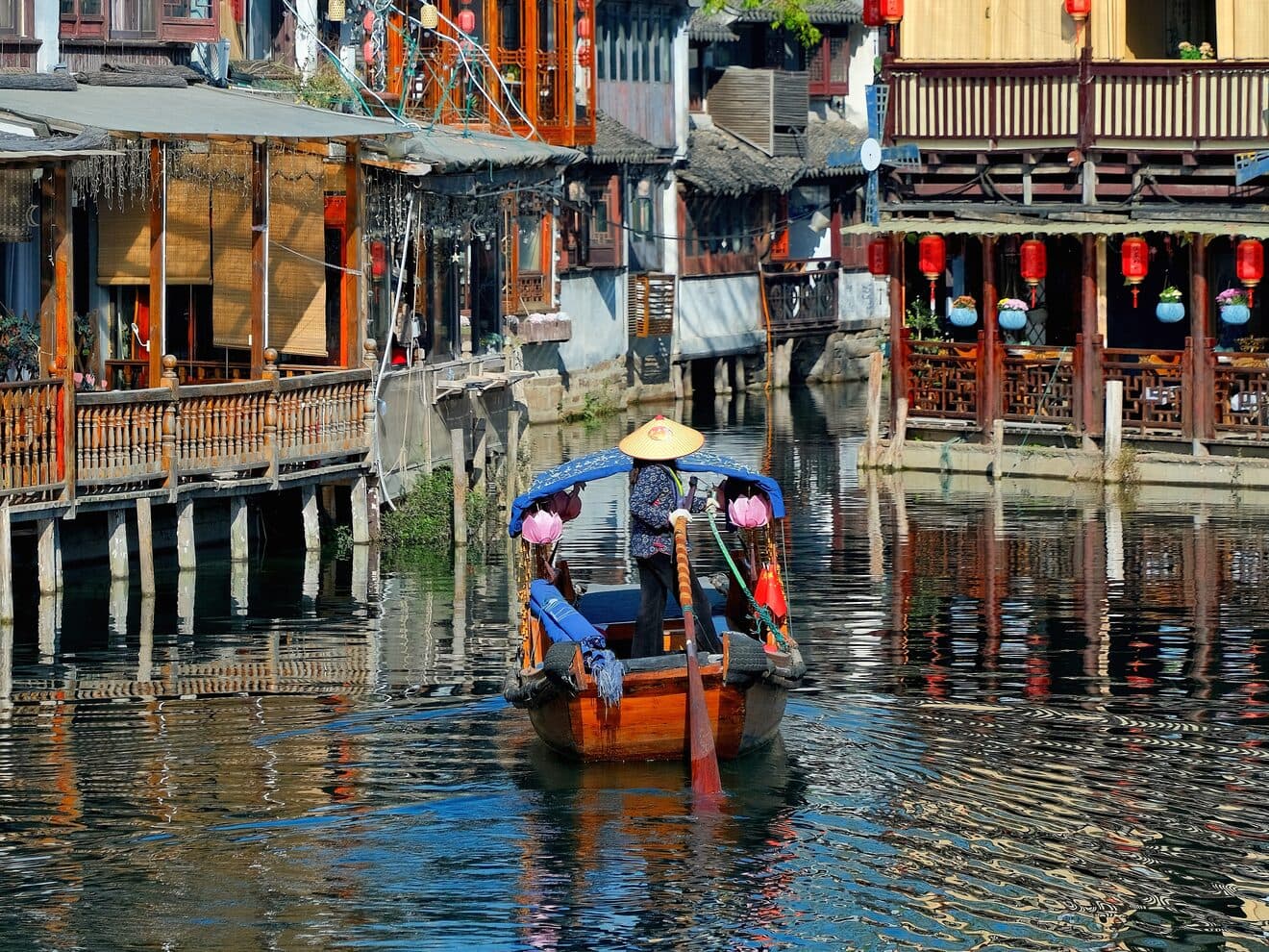 A covered boat moving through a Suzhou water-town canal between white-walled, grey-tiled houses