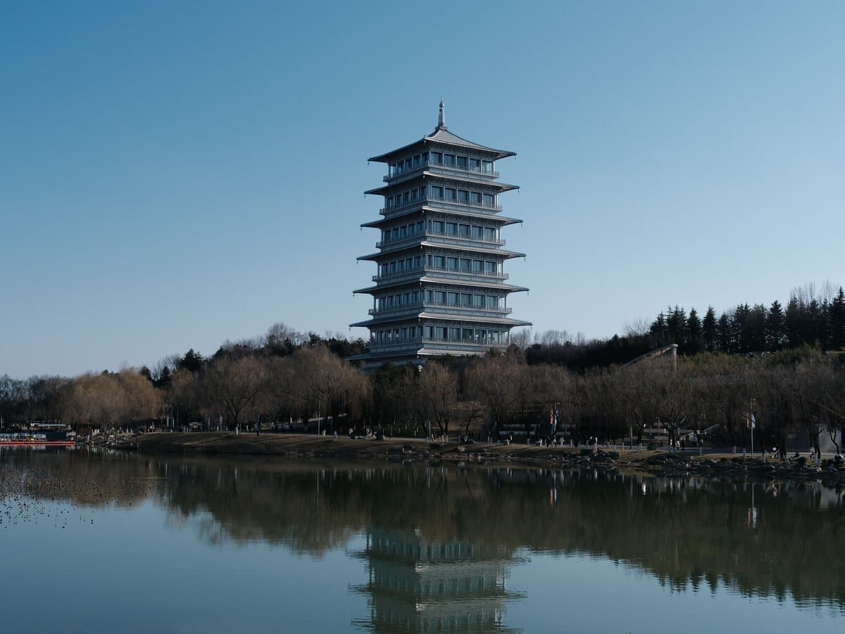 A multi-storey pagoda across a lake, mirrored in the water among bare trees under a blue sky