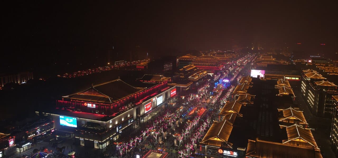 An aerial night view of a Tang-style district with rows of Tang-inspired roofs and lit streets below city blocks
