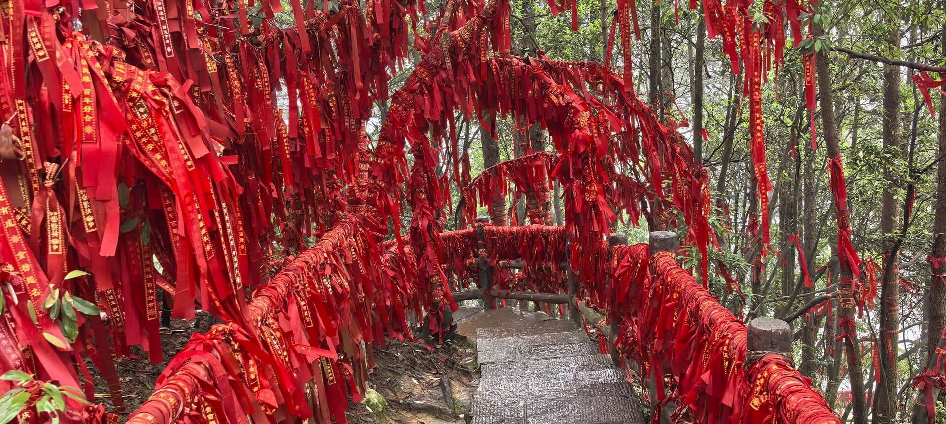Forest path railing covered with red prayer ribbons