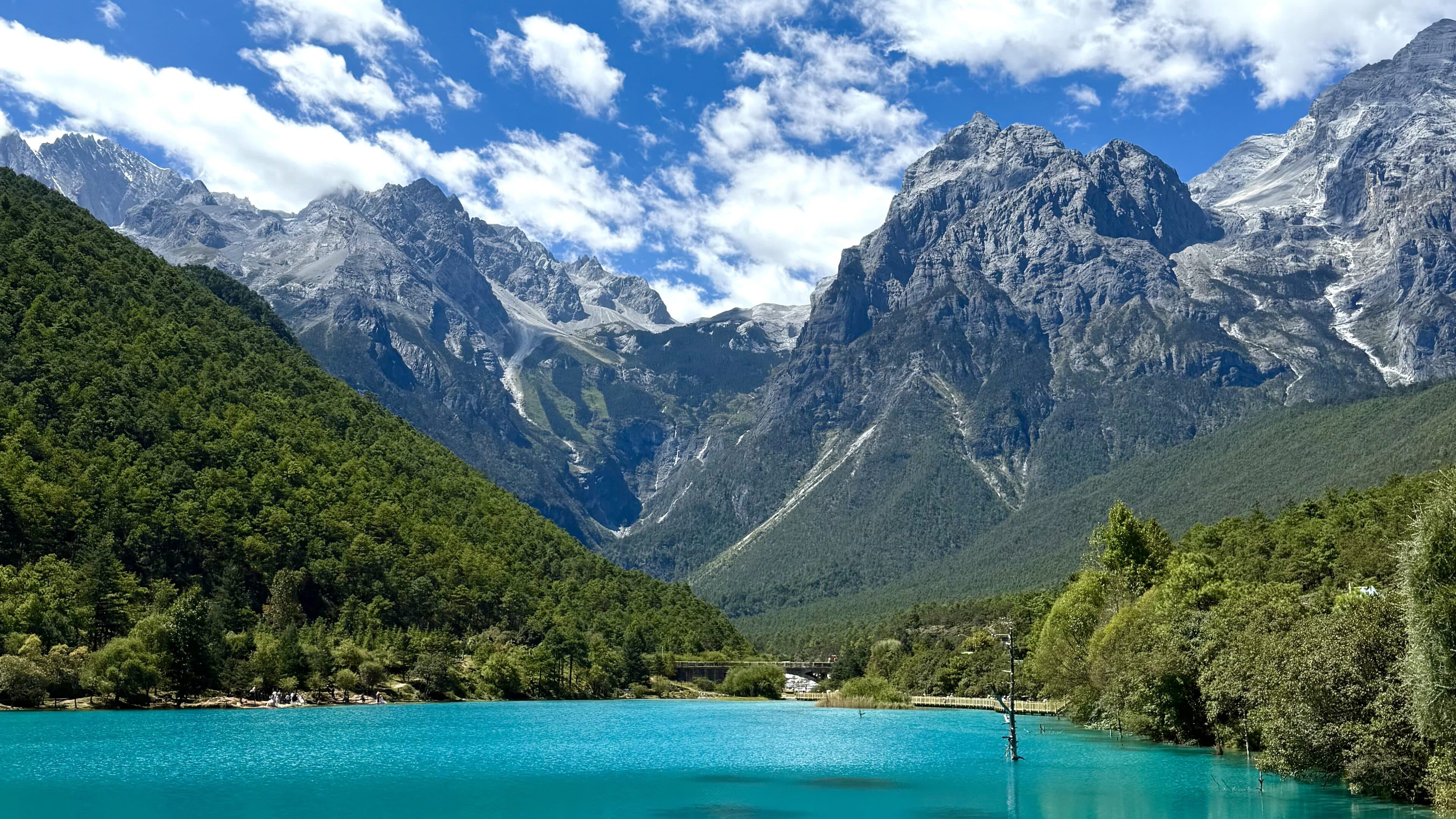 Blue-green lake water below rocky peaks with pine trees on the far bank