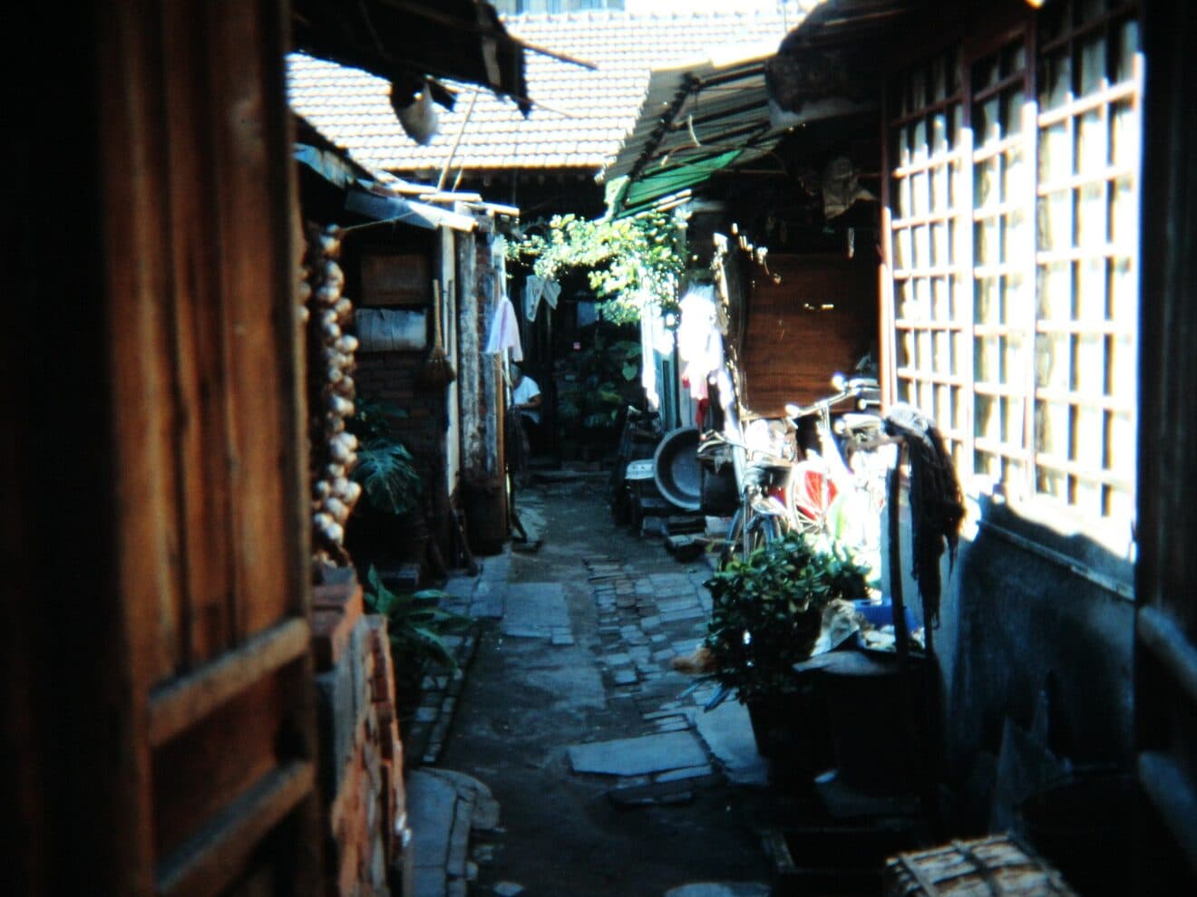 A Beijing hutong lane: grey brick walls and courtyard gates along the alley, a bicycle parked against one wall