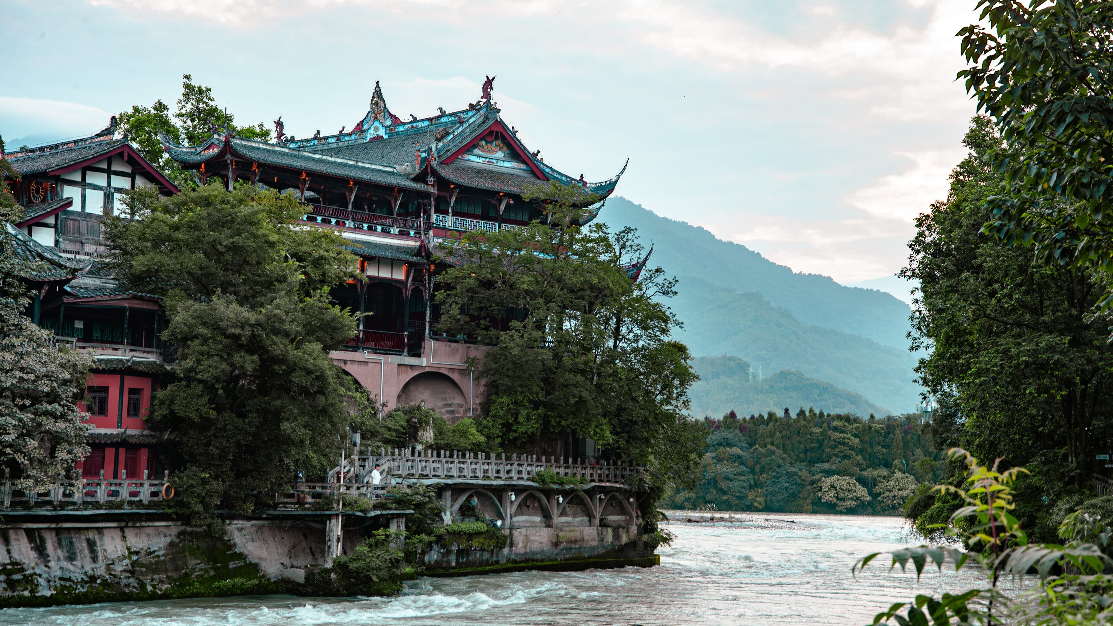 A multi-storey Chinese pavilion with green tiles and red columns, stone balustrades and trees
