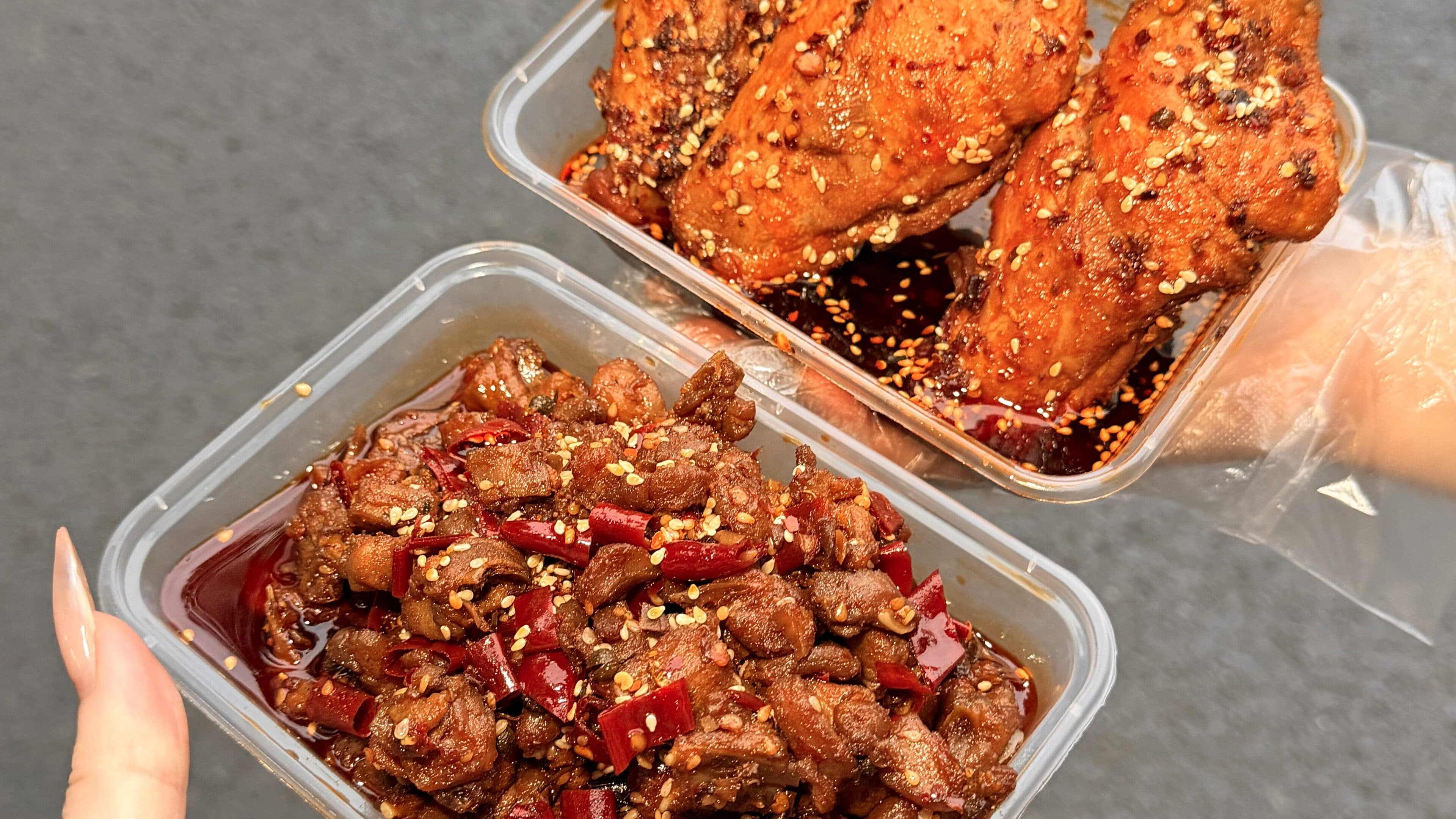 Two boxes of chilli-oil braised meat with dried chilli and sesame, held in hand