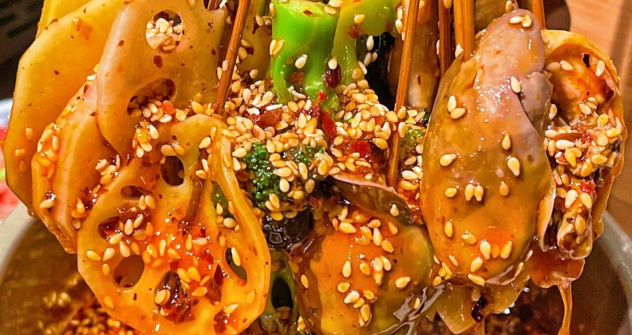 Skewers in chilli oil with lotus root, broccoli and meat, scattered with sesame
