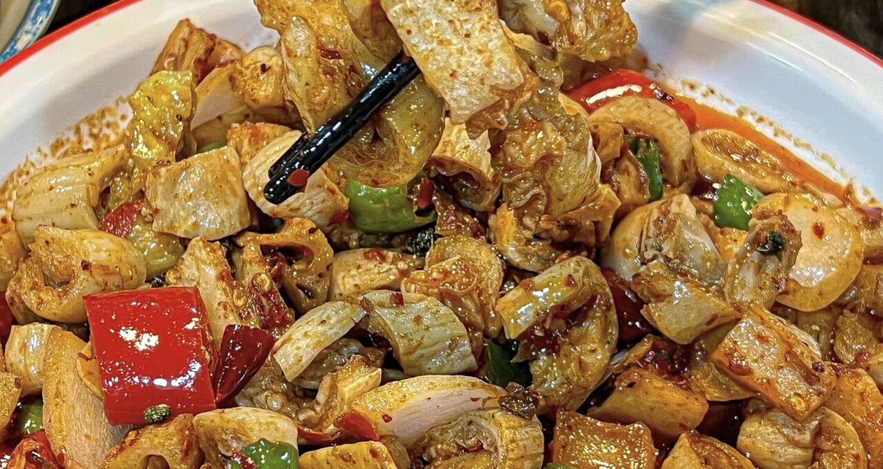 A Sichuan dish in chilli oil with peppers and pieces of meat, one lifted with chopsticks