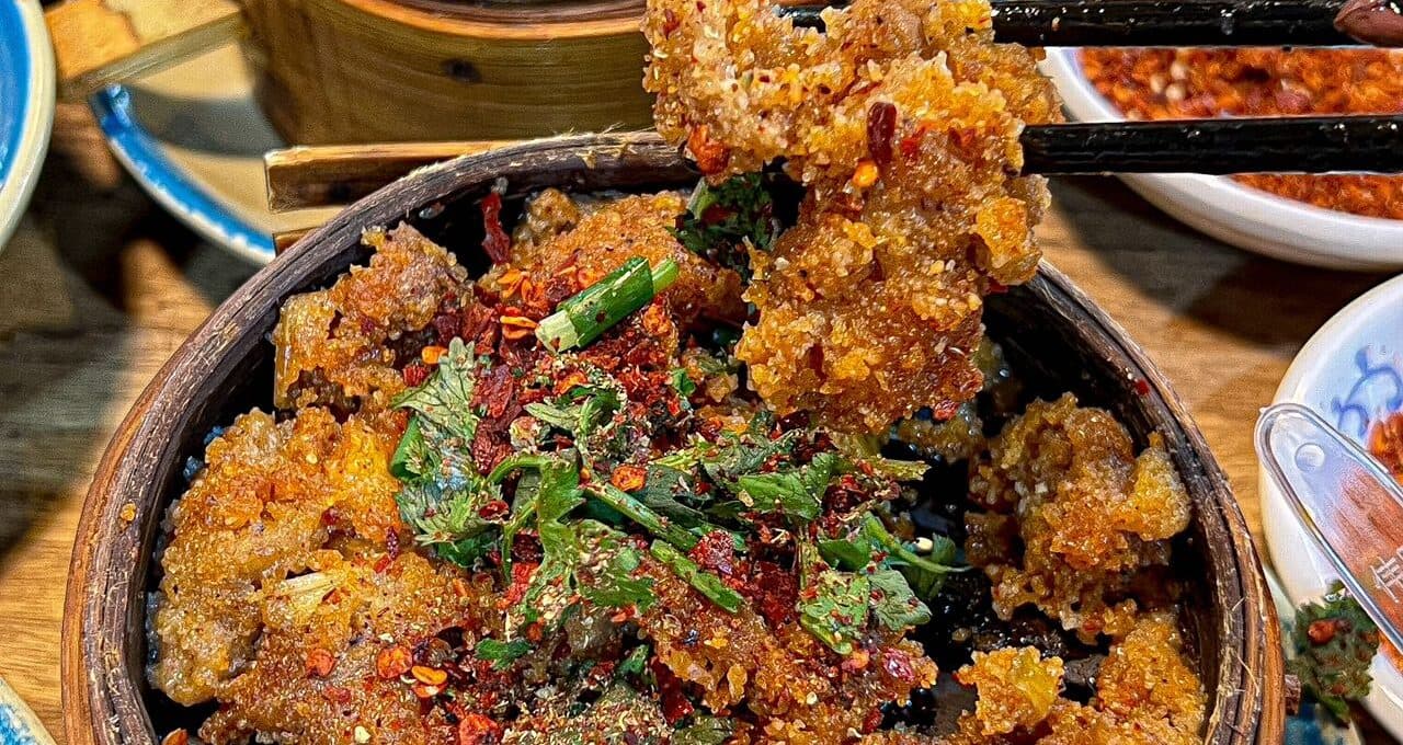 Steamed dishes in a bamboo steamer, a piece lifted with chopsticks, a chilli dip behind