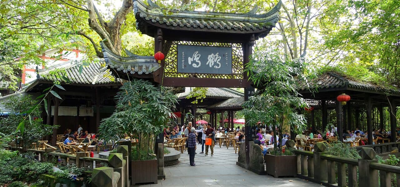 The old teahouse in Chengdu's People's Park: a tiled gateway with its inscribed board among trees, tea tables set out across the courtyard