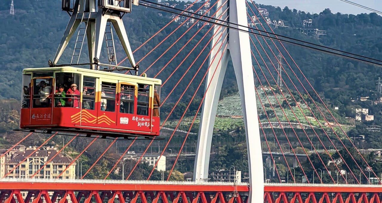 The Yangtze cableway car crossing the river, with the red bridge and hillside blocks behind