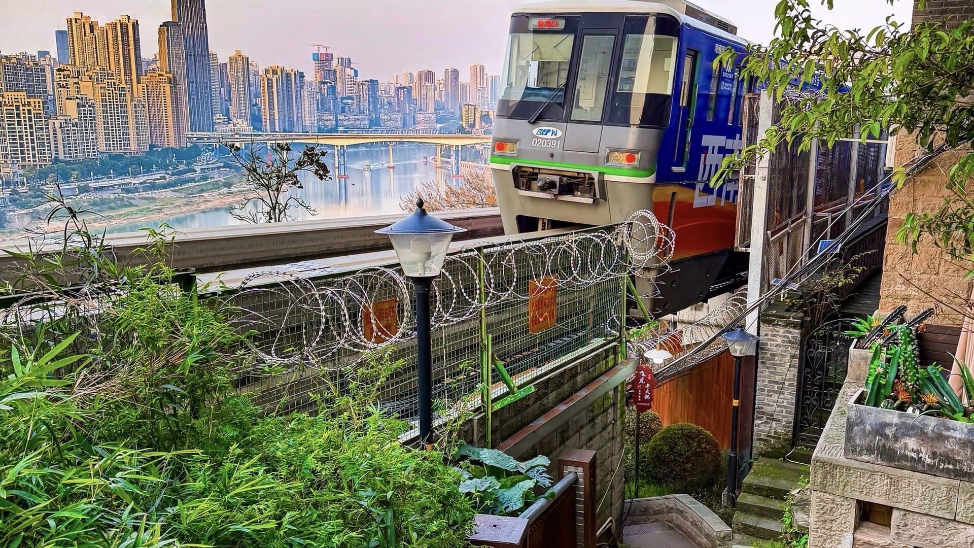 A hillside walkway in Chongqing by day: stone steps and railings climbing past a monorail threading between blocks and trees