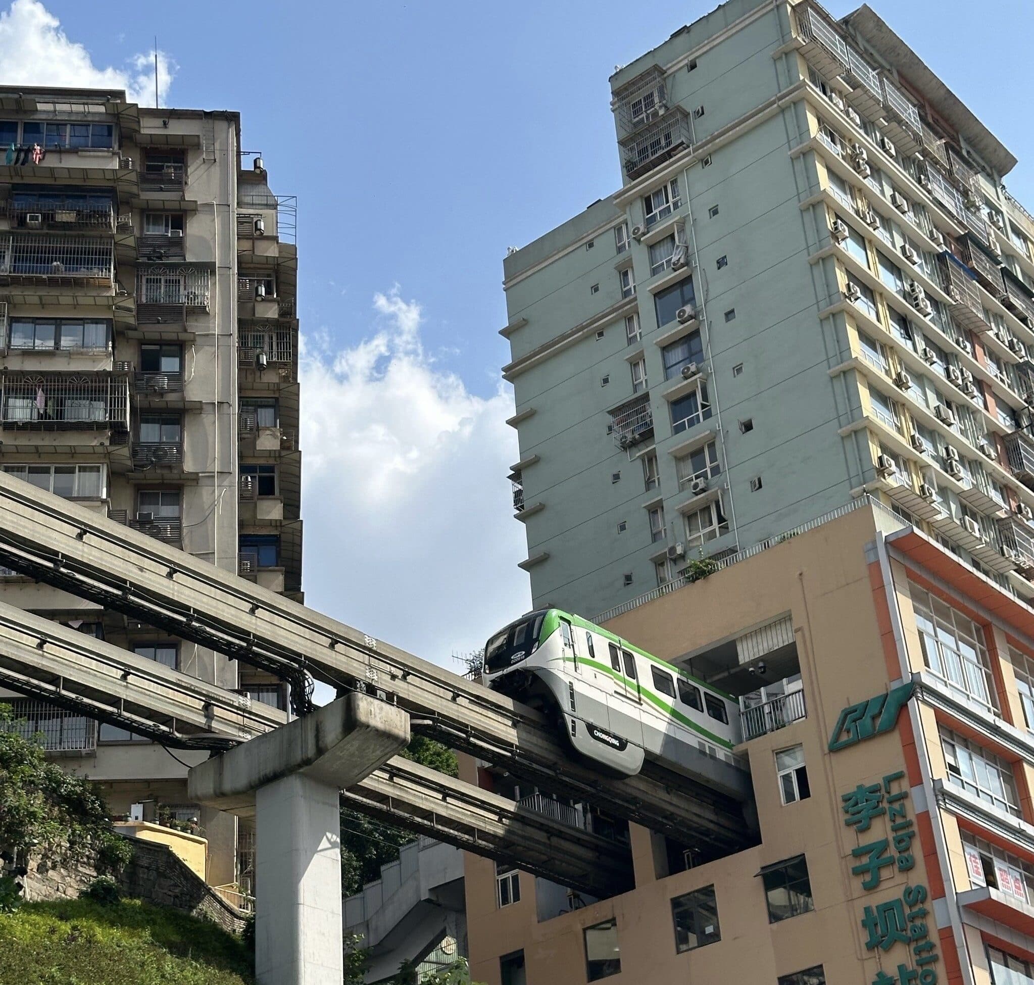 Liziba station in Chongqing by day: a monorail train passing through the floors of a residential block, with trees and the street below