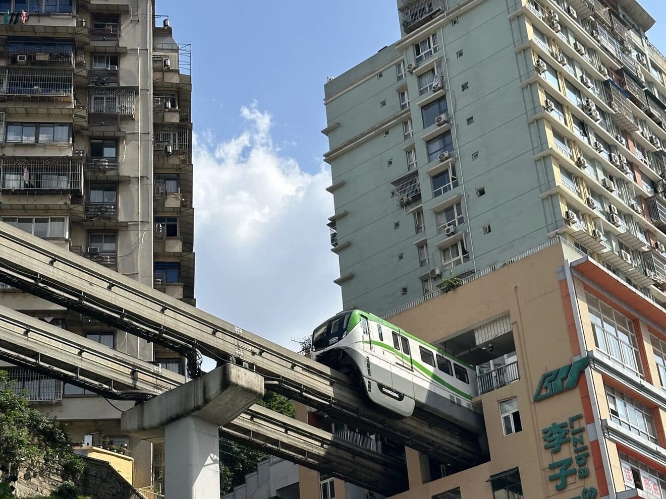 A monorail train passing through a residential block, its elevated track climbing the slope