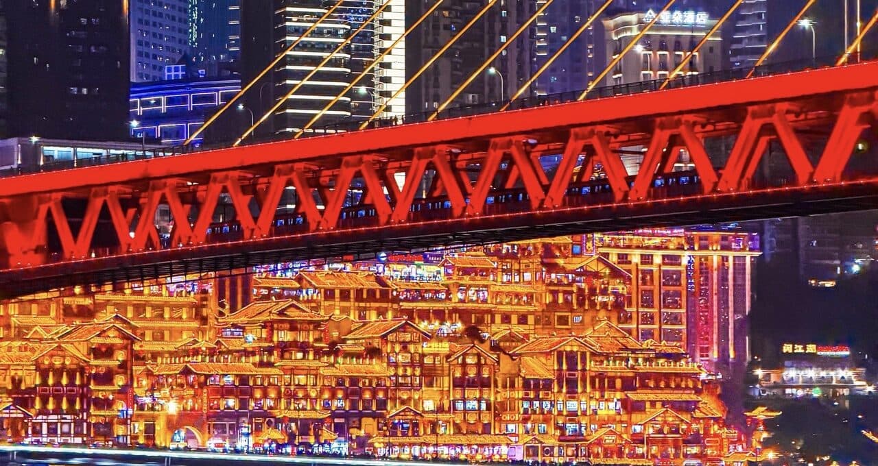 Hongyadong's lit stilt-house tiers at night with the red bridge and its river reflection