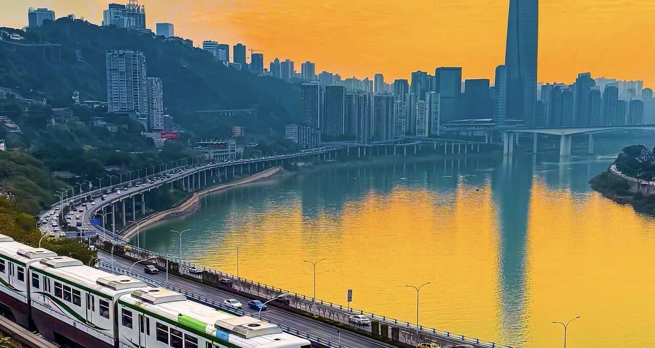 A monorail train crossing the river bridge at golden hour, city towers along the far bank