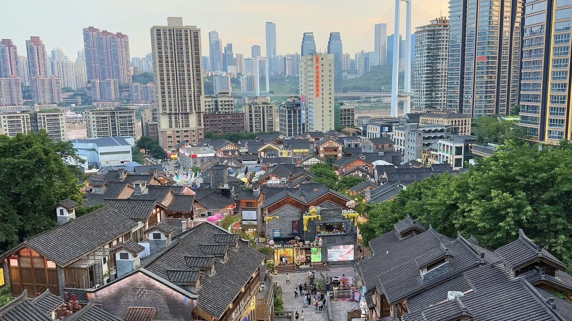 Hongyadong by day: tiered stilt-house roofs and timber eaves with modern towers across the Jialing River behind