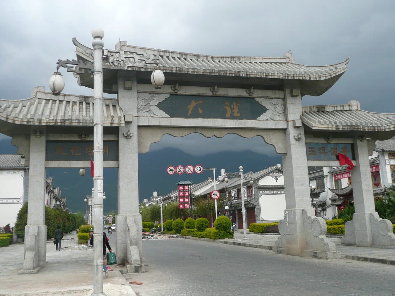 The stone archway at the entrance to Dali old town, its inscribed board against cloud over the Cangshan range