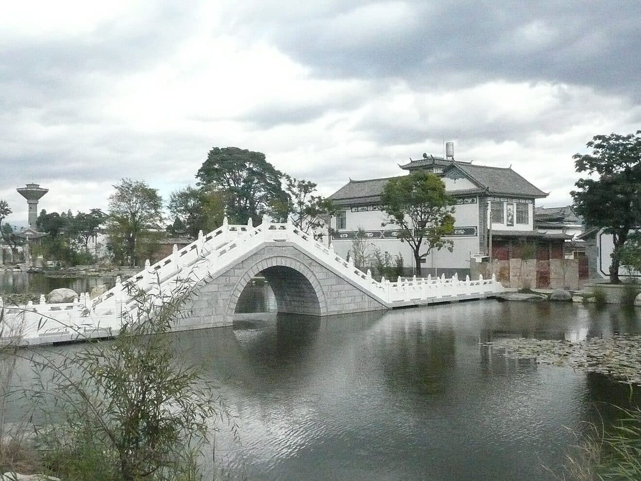 Xizhou old town: a stone arch bridge over a pond with Bai-style white-walled, grey-tiled houses behind