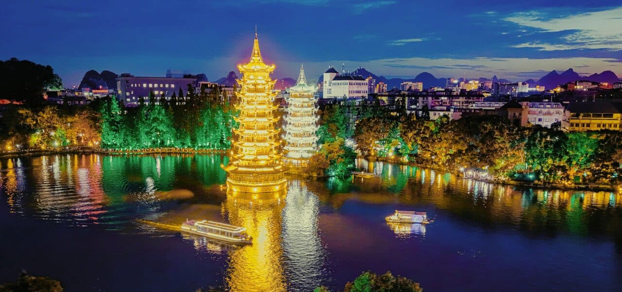 Guilin by night: two illuminated towers mirrored in the lake, with shoreline lights and boats along the bank