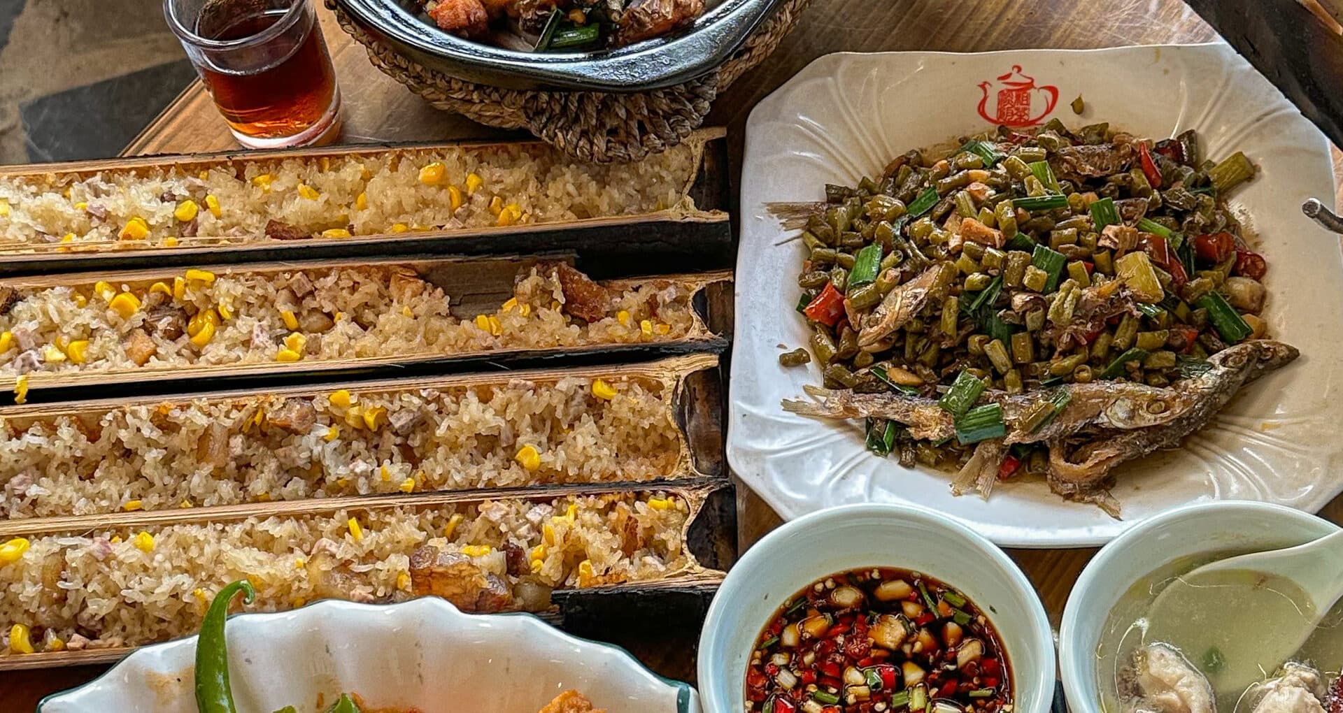 A countryside table with bamboo-tube rice, river fish and stir-fried greens, dipping dishes alongside