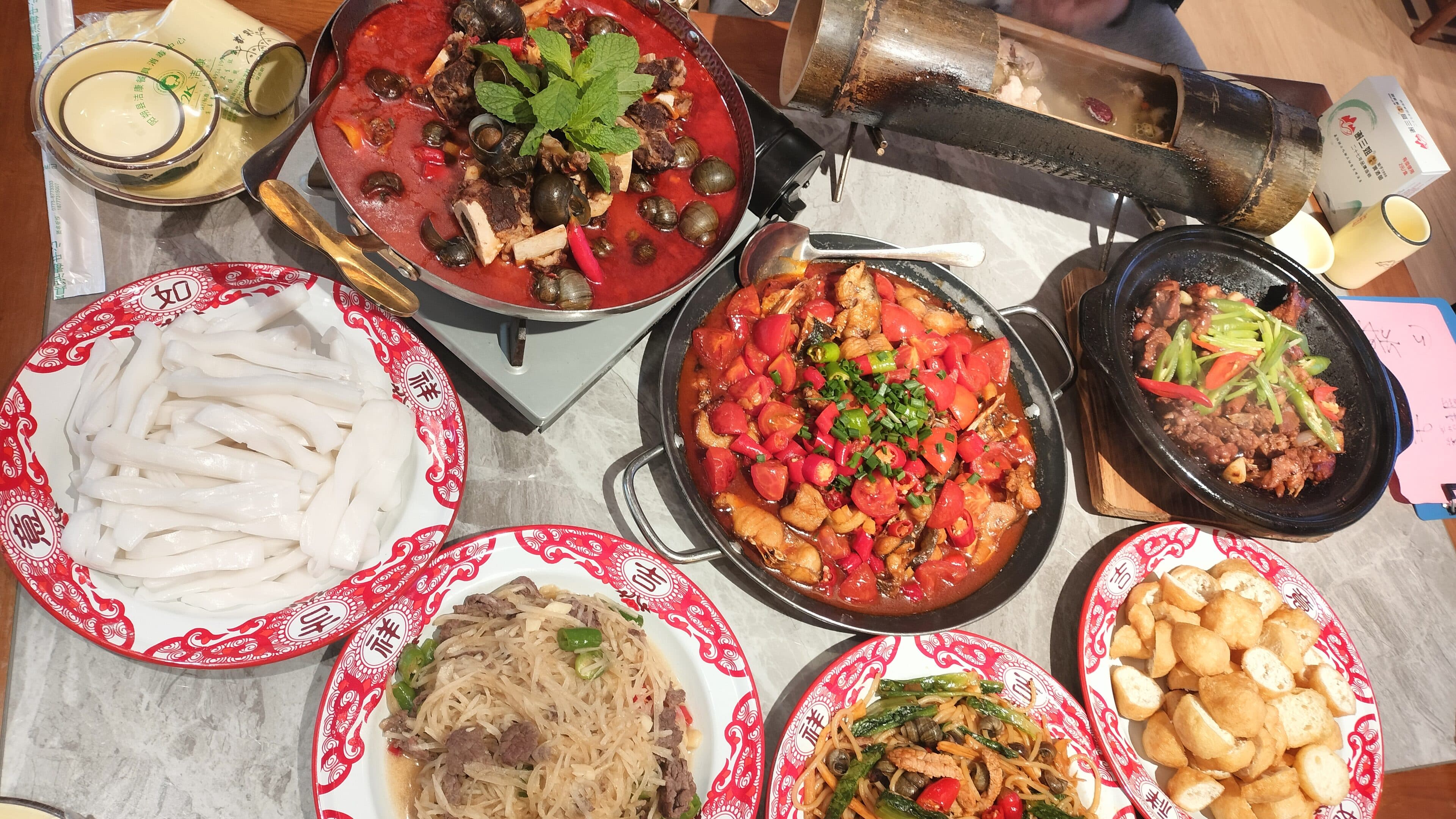An overhead view of a full table of Chinese dishes, with a portable stove pot and griddle