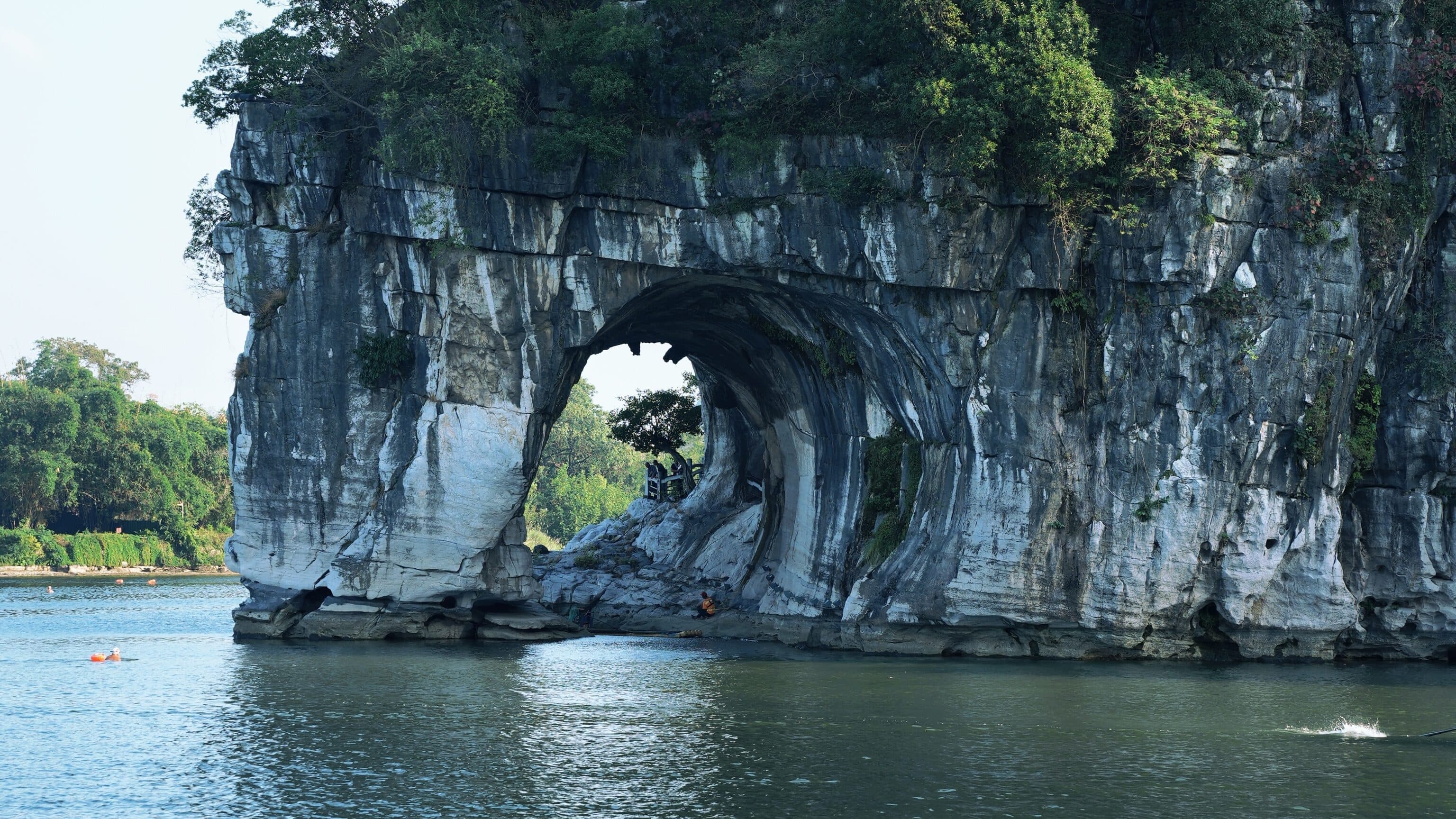 Elephant Trunk Hill in Guilin: the Water-Moon Cave arch cut through the riverside cliff below dense greenery, the hill reflected in the open river below