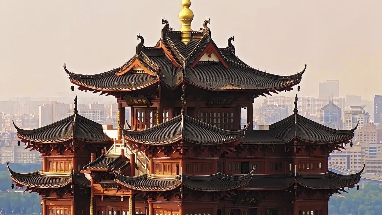 A multi-tiered traditional pavilion at dusk above city rooftops under a pale pink sky