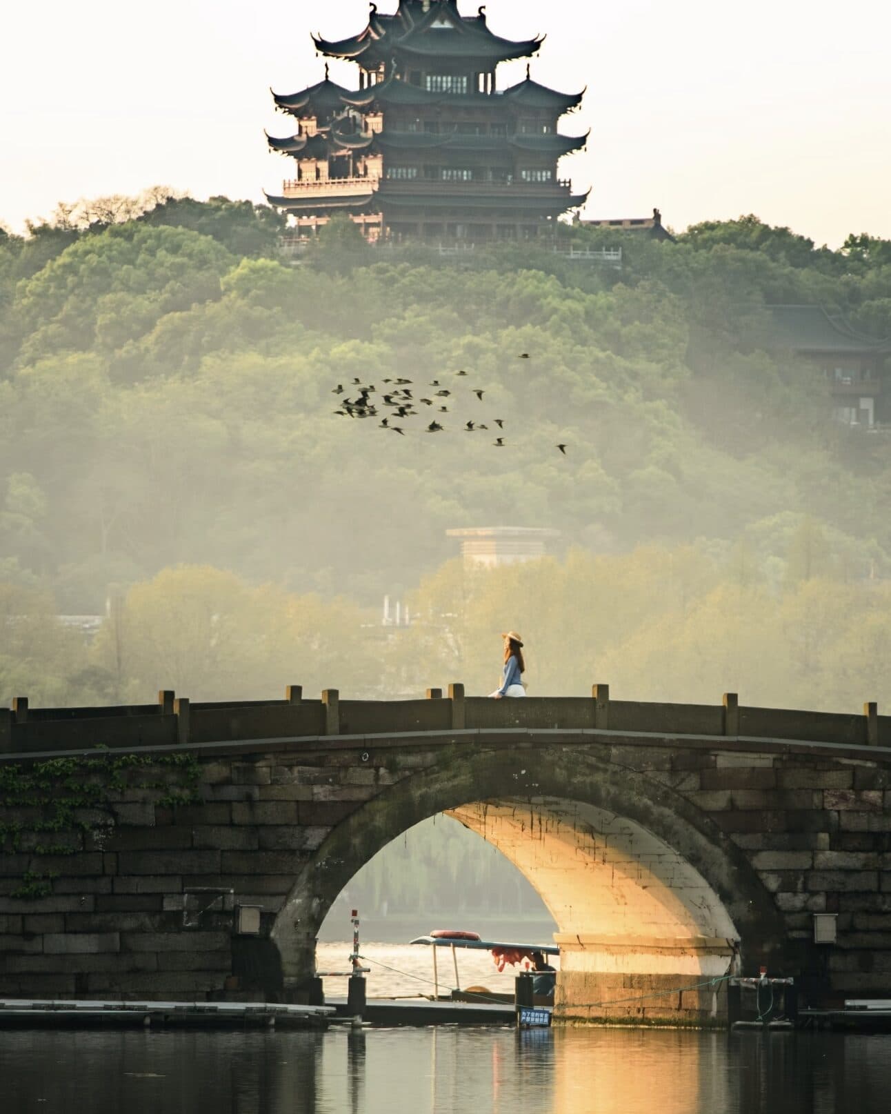 A stone arch bridge with a single walker in morning mist, wooded slopes above