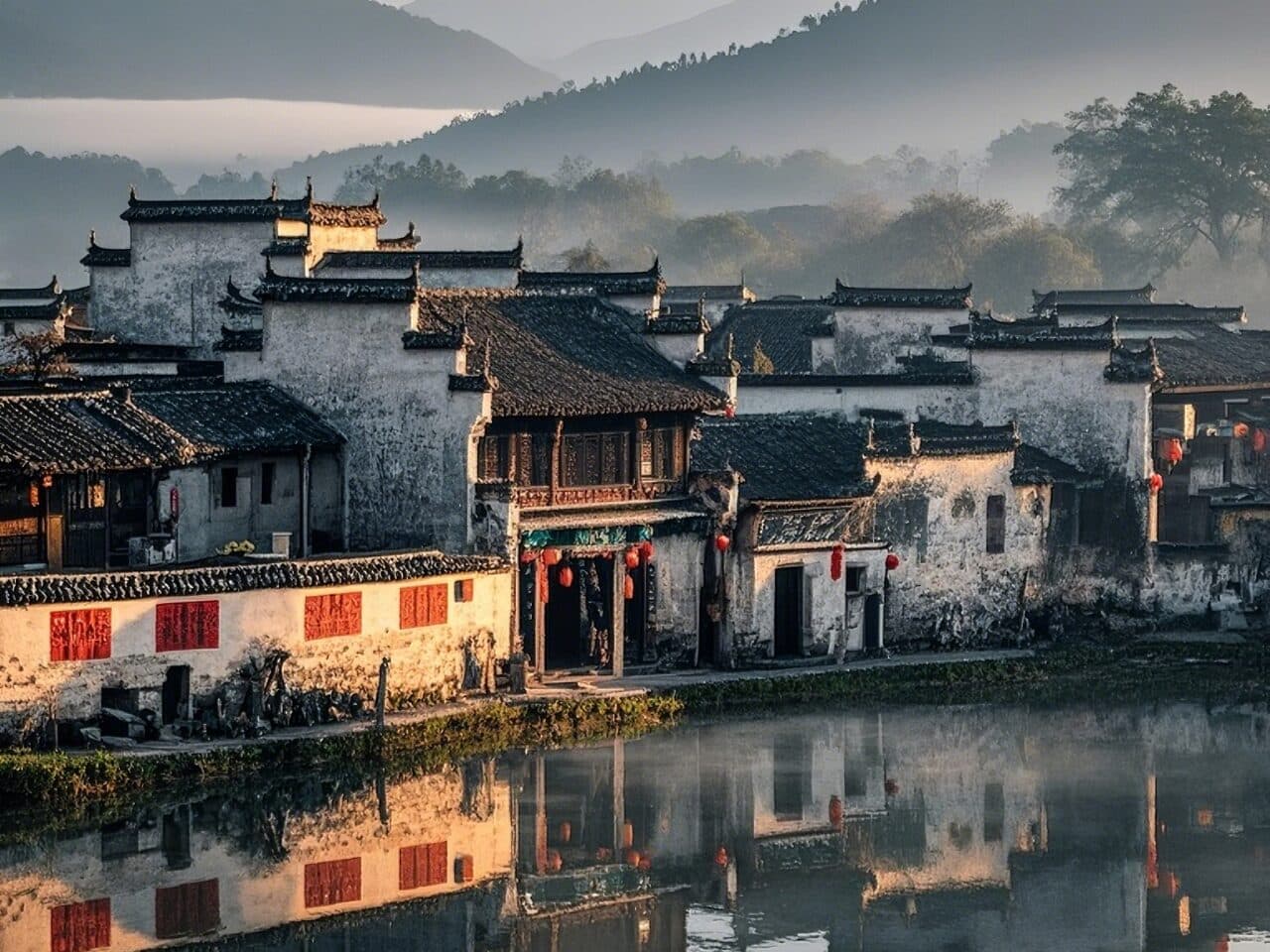 Hui-style village houses with dark tile roofs and red lanterns reflected in still water, hills in haze behind