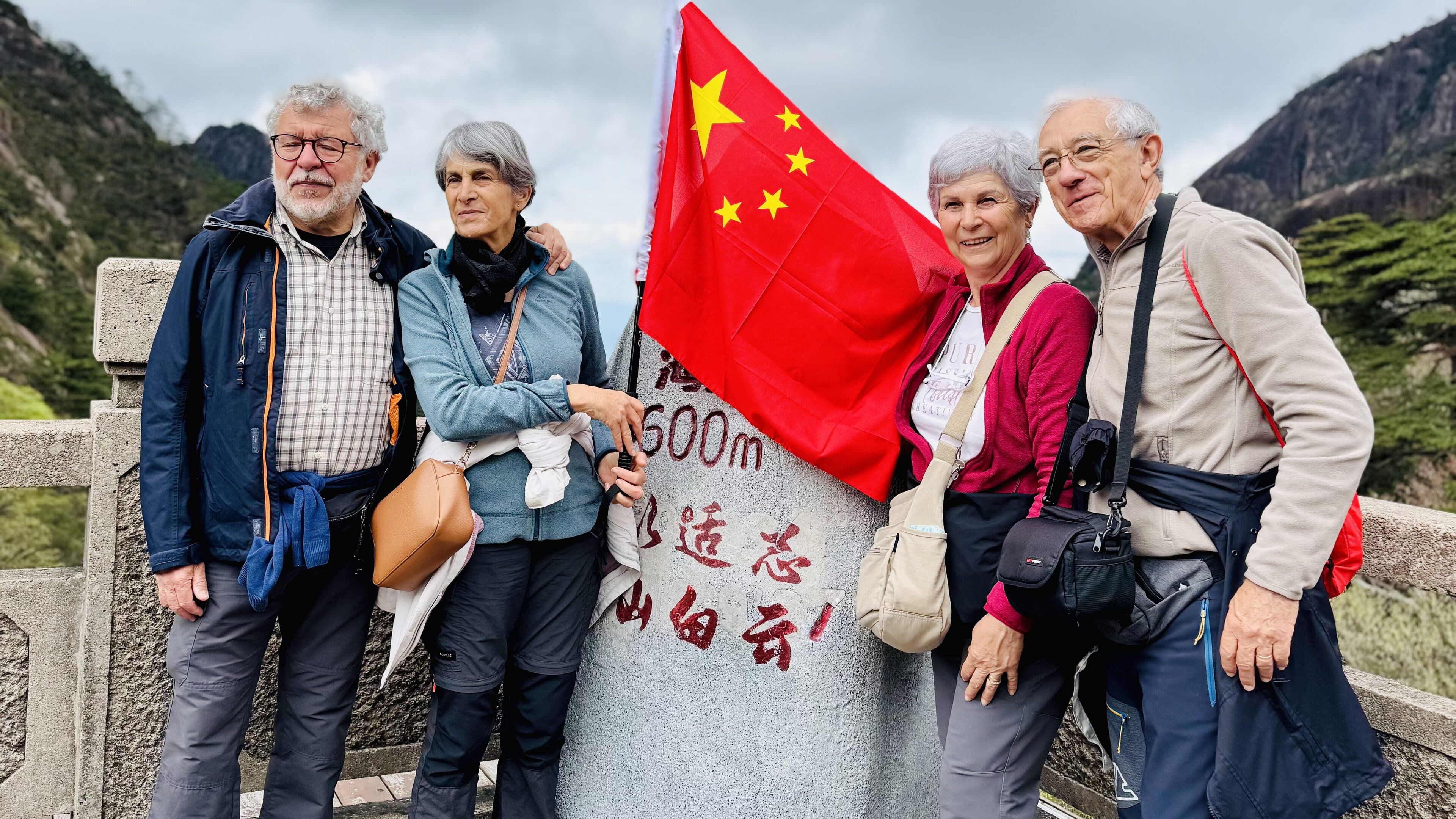 Four older visitors with a flag at a summit stone balustrade marked 500m