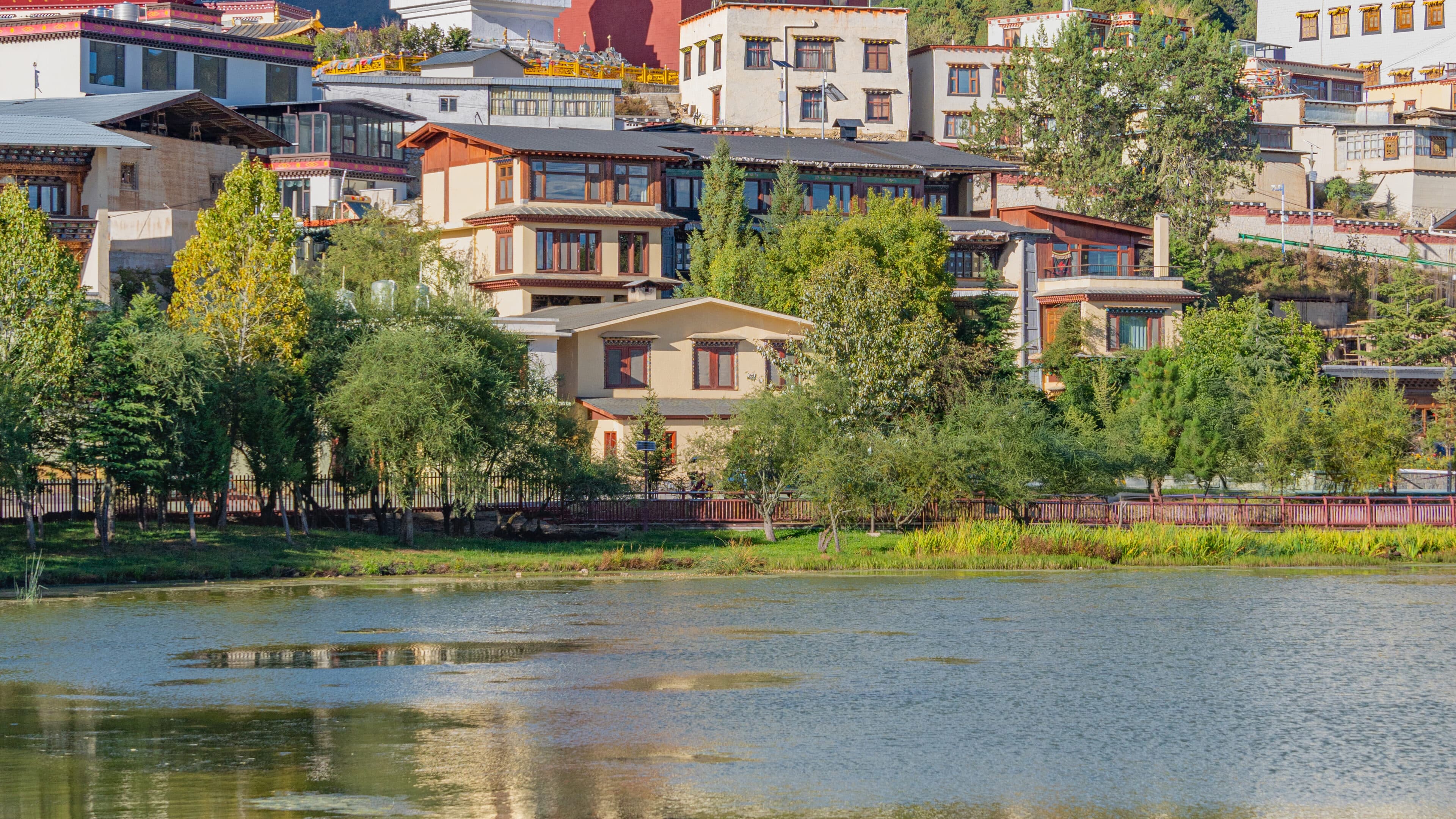 Waterside trees and Tibetan-style buildings behind a timber fence