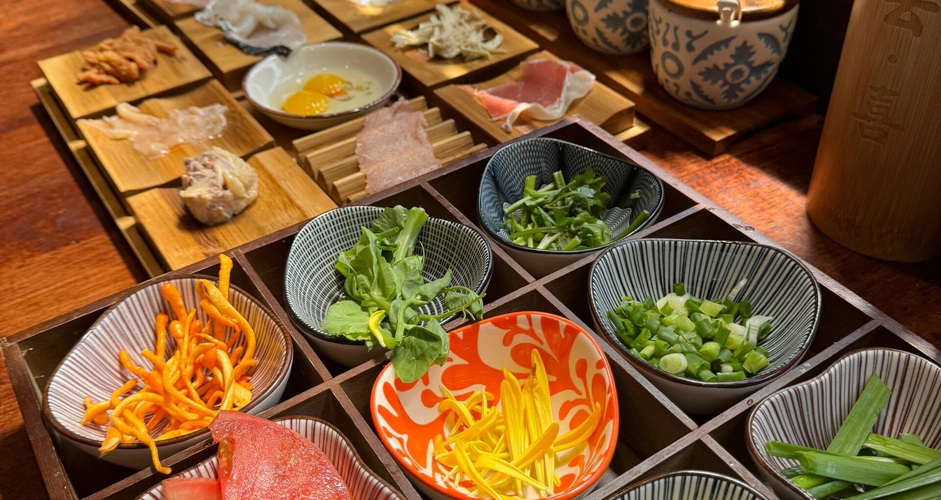 A wooden tray of side dishes for crossing-the-bridge noodles: small plates of meat, egg and vegetables