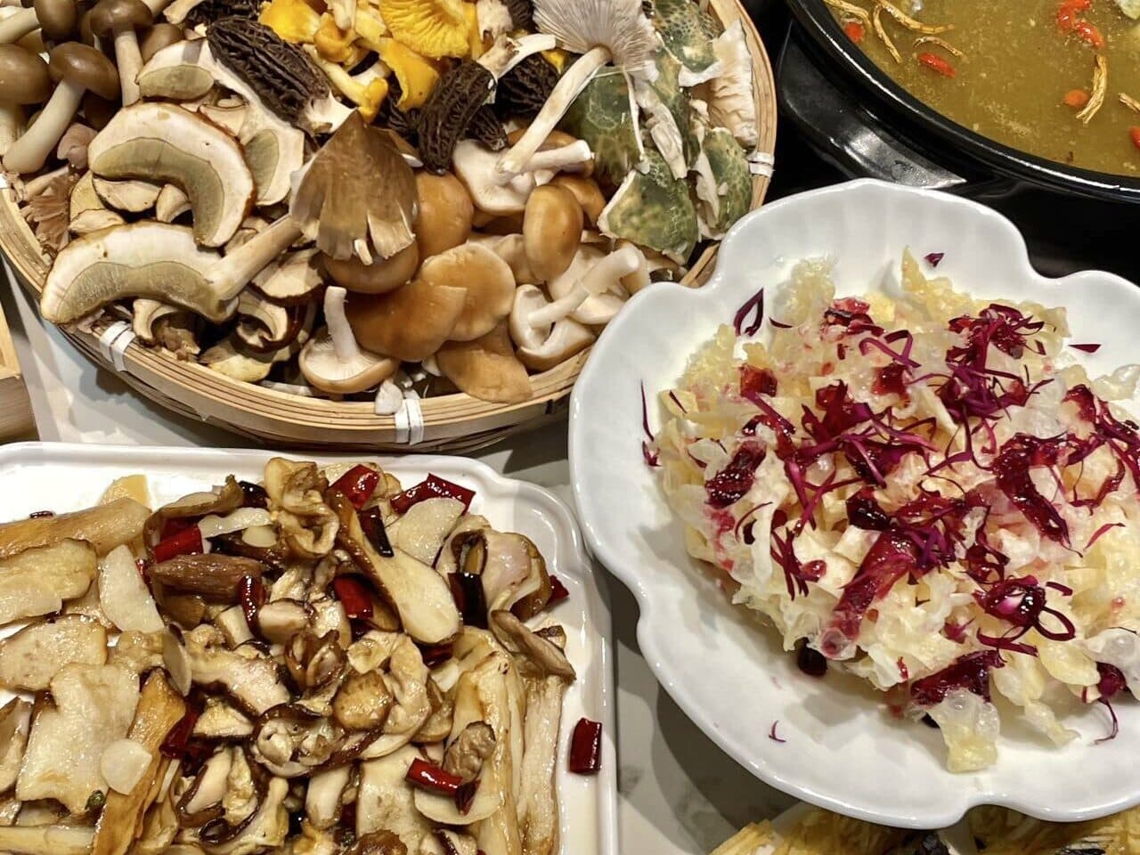 A mushroom meal: fresh mushrooms in a basket with plated mushroom dishes and a pot of broth
