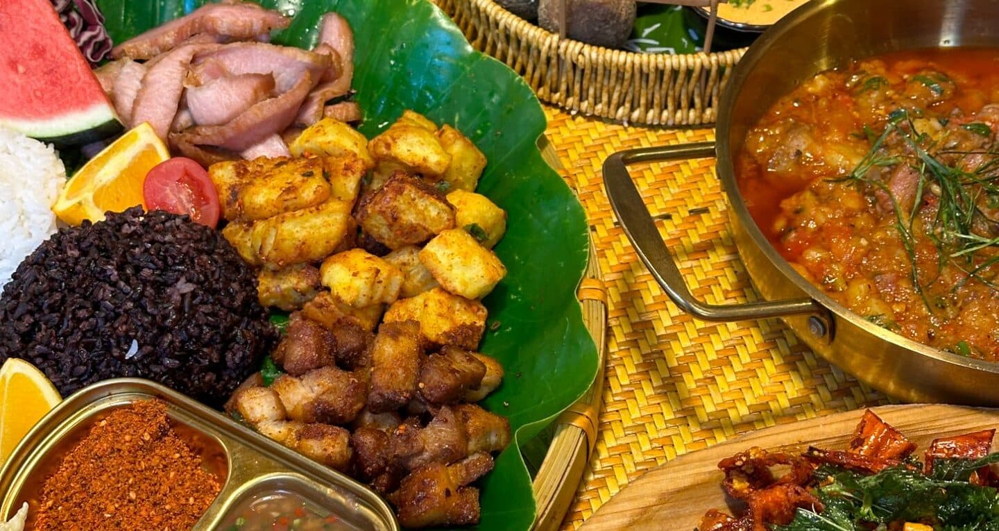 A Yunnan spread on a banana leaf: purple rice, fried dishes and fruit beside a pot of soup