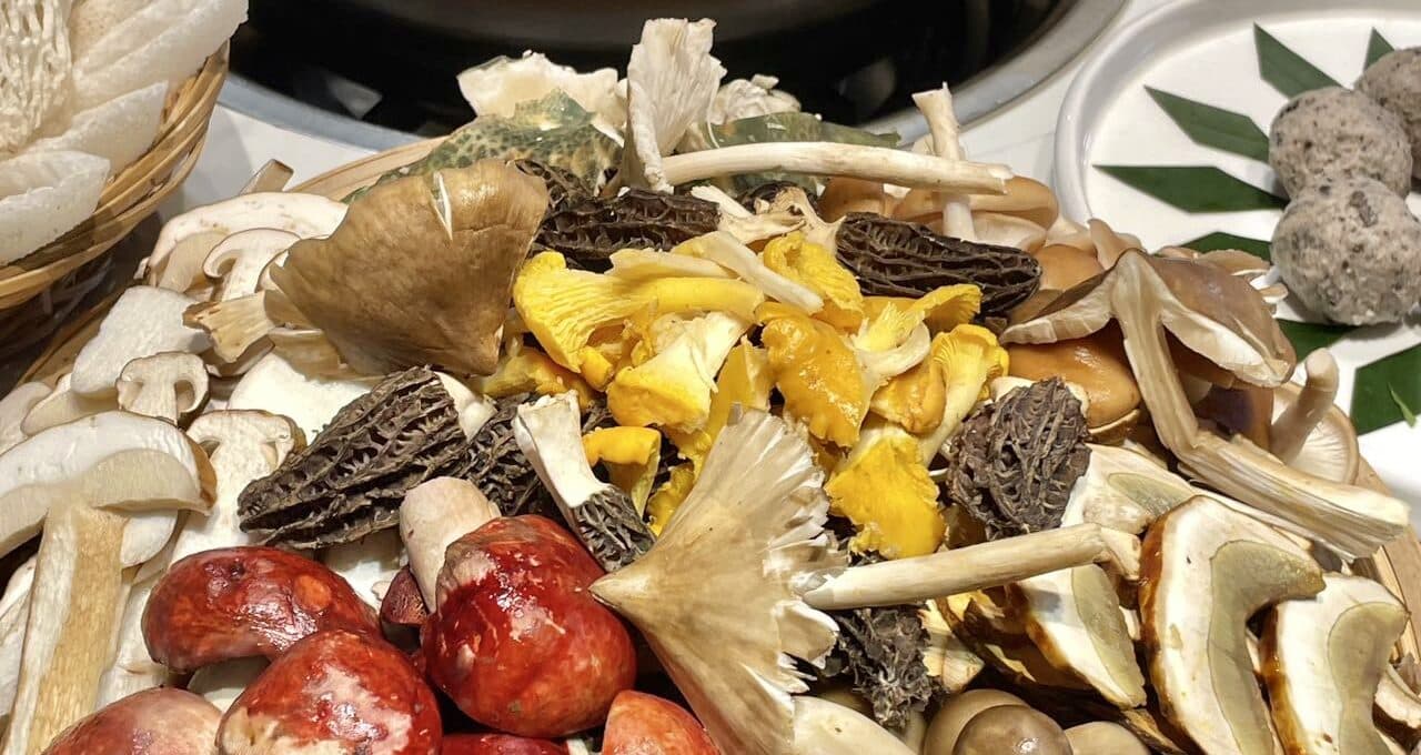 Fresh mushrooms in a bamboo basket beside a dark pot of soup