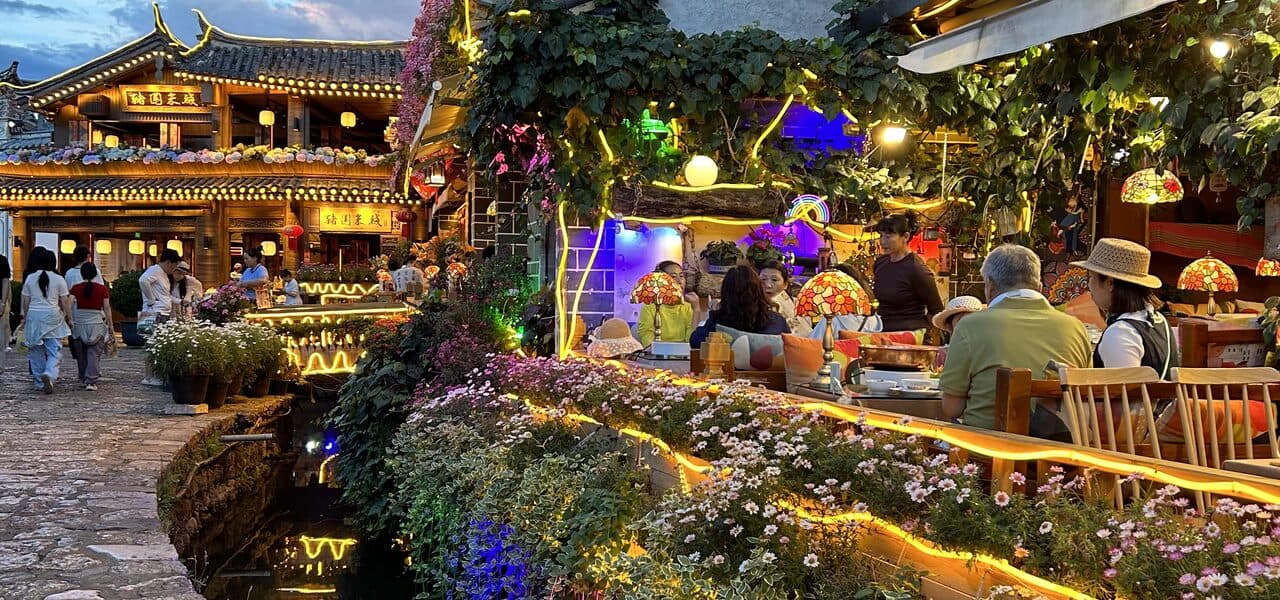 Lijiang old town's canal at dusk: red lanterns, bougainvillea and lit tables along the water