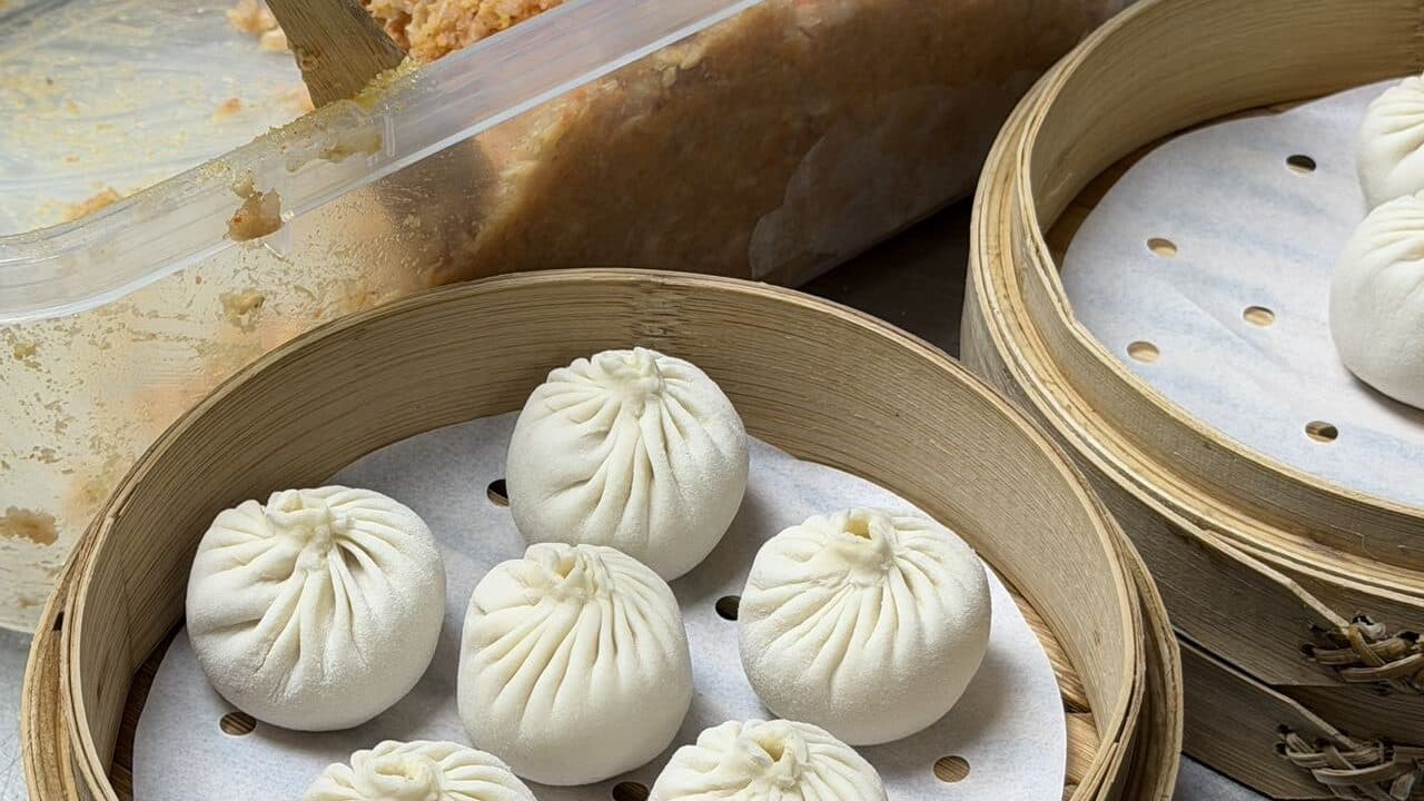 White xiaolongbao and buns in stacked bamboo steamers, their pleated tops in clear view